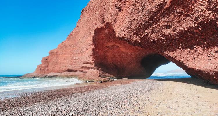 L'arche spectaculaire de grès rouge s'étend au-dessus de l'océan turquoise et de la plage de galets.