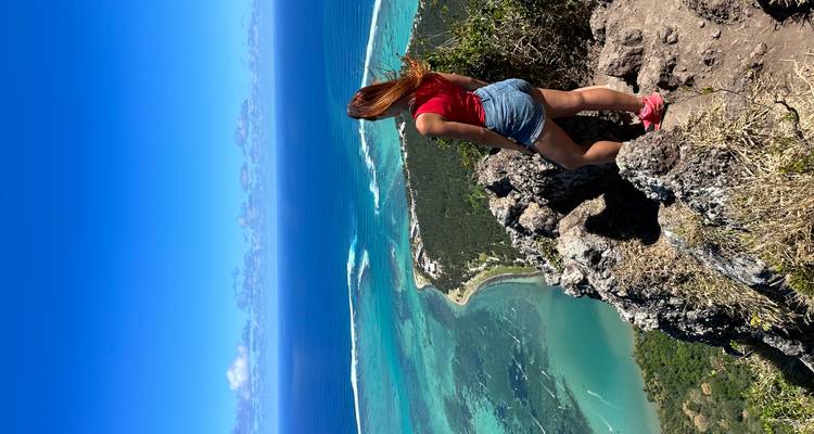 A hiker stands on a rocky peak overlooking the vivid blue lagoon and reefs off Le Morne peninsula.