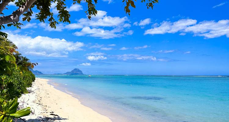 Pristine white-sand tropical beach with clear turquoise water and Le Morne mountain on the horizon under a bright blue sky.