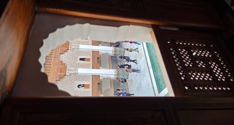Binnenplaats van Ben Youssef Madrasa gezien door een raam met boogvormig traliewerk met toeristen eronder.