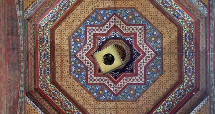 Symmetrisch, rijkelijk beschilderd achthoekig plafond met ingewikkelde geometrische en bloemmotieven van onderaf bekeken.