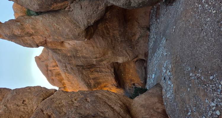 Smalle rotsige doorgang met hoge oranje canyonwanden en verspreide stenen op de grond.