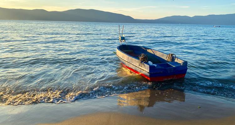 Bote de pesca de madera solitario flotando en un mar tranquilo al atardecer con las montañas de fondo.