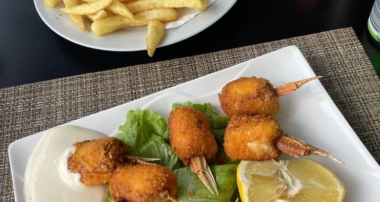 Plato de trocitos de mariscos fritos con papas fritas y una rodaja de limón en una mesa de restaurante.