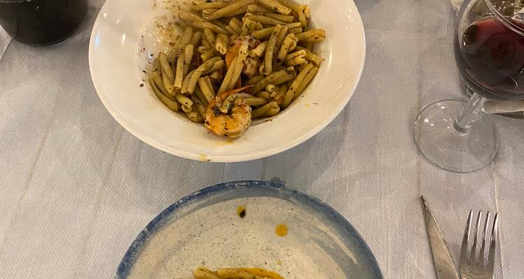 Bol de pâtes au pesto à moitié consommé avec crevettes et un verre de vin rouge sur la table.