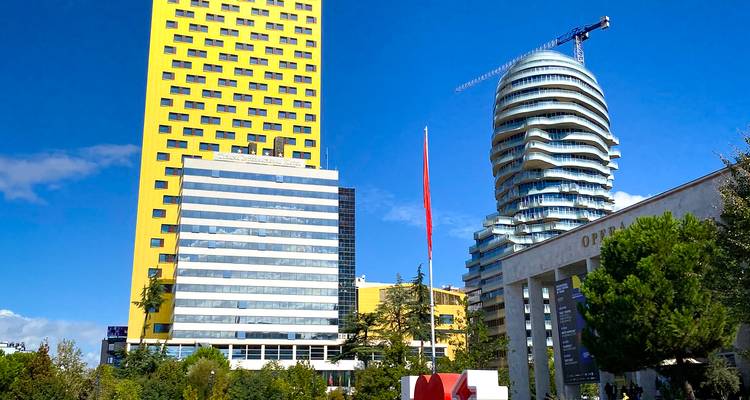 Skyline moderne de Tirana présentant une tour jaune vif et un gratte-ciel en verre aux formes courbes.
