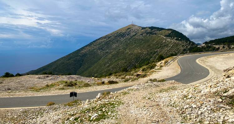 Une route de montagne sinueuse épouse les contours d'une pente rocheuse sous un ciel partiellement nuageux.
