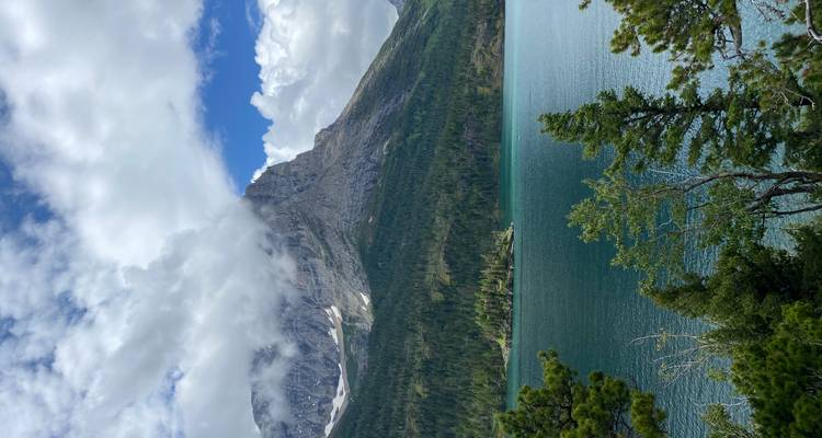 Smaragdgrüner Bergsee, umgeben von Kiefernwäldern mit einem majestätischen, wolkenumhüllten Berg dahinter.