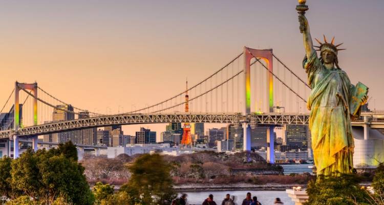 Die Freiheitsstatue-Replik in Odaiba mit der Rainbow Bridge und der leuchtenden Skyline bei Sonnenuntergang.