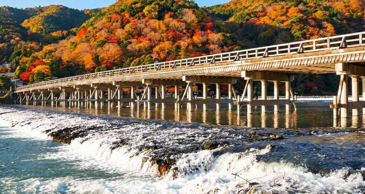 Herbstliche Farben rahmen die Togetsukyo-Brücke ein, die sich über einen glitzernden Fluss in Kyoto erstreckt.