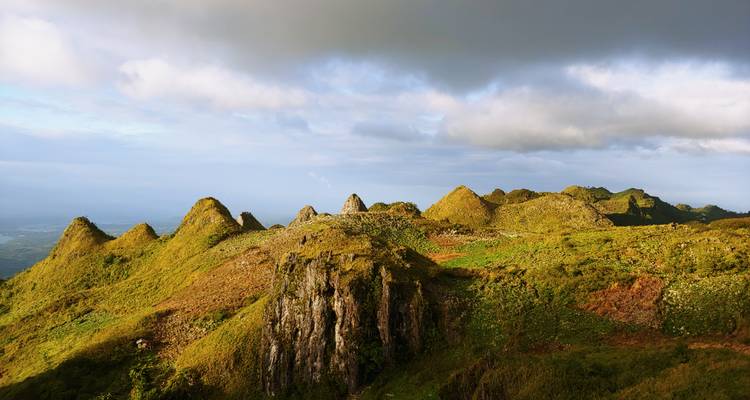 Sunlit ridge of jagged hills under dramatic clouds with expansive views.