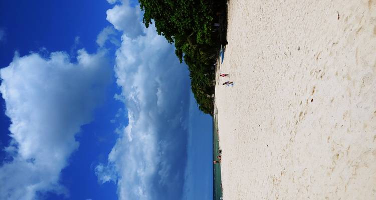 Wide, empty stretch of white sand beach with a few visitors under dramatic clouds.