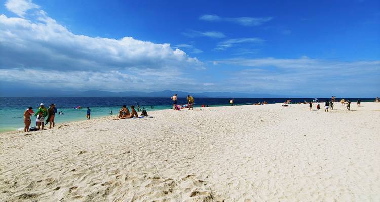 Sandbar-like beach jutting into the sea with sunbathers and swimmers enjoying clear weather.