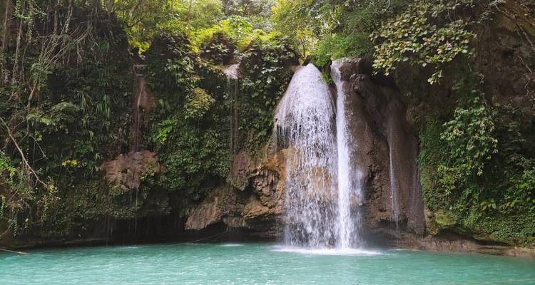 Broad waterfall pouring into a striking turquoise pool amid dense greenery.