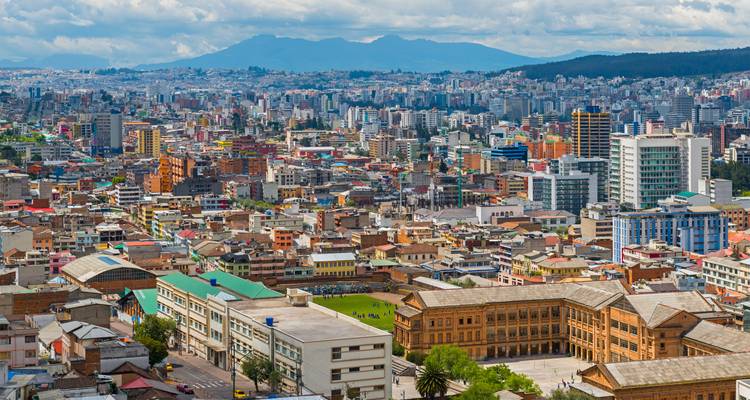 Paysage urbain dense de bâtiments modernes et coloniaux à Quito avec des pics volcaniques lointains.