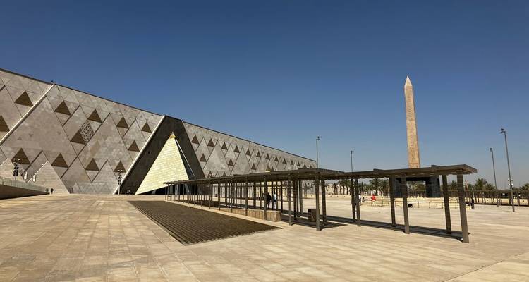 Façade angulaire moderne du Grand Musée égyptien à côté d'un haut obélisque sous un ciel bleu dégagé.