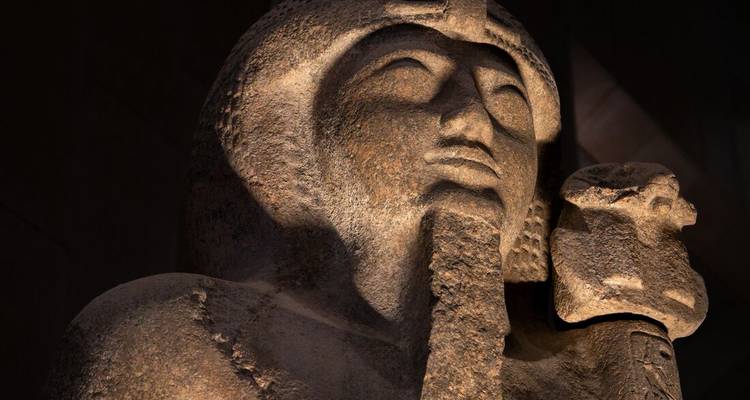 Gros plan d'une statue antique en granit d'un pharaon dramatiquement éclairée à l'intérieur d'un musée.