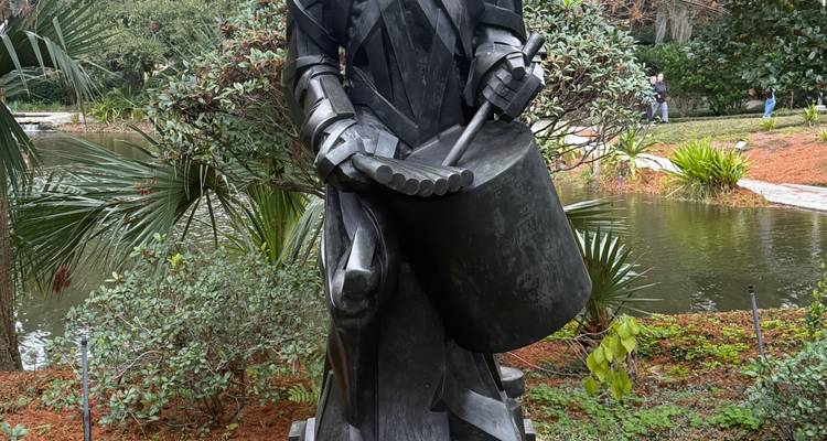 Sculpture de garçon tambour métallique se tenant près d'un étang au milieu de plantes tropicales luxuriantes dans un jardin.
