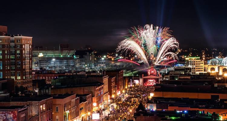 Nächtliche Skyline von Nashvilles Broadway, gefüllt mit Feiernden und lebhaften Feuerwerken, die den Himmel erleuchten.