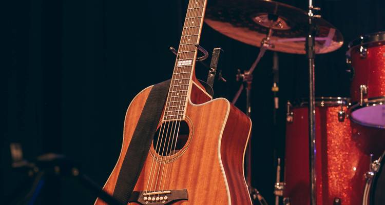 Akustische Gitarre auf einer schwach beleuchteten Bühne mit einem unscharfen Schlagzeug im Hintergrund.