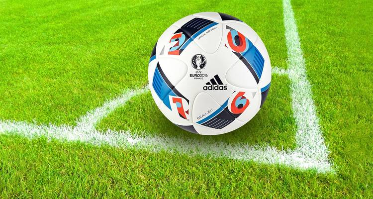 Primer plano de un balón de fútbol Adidas Euro 2016 descansando en la esquina del terreno de juego de color verde brillante.