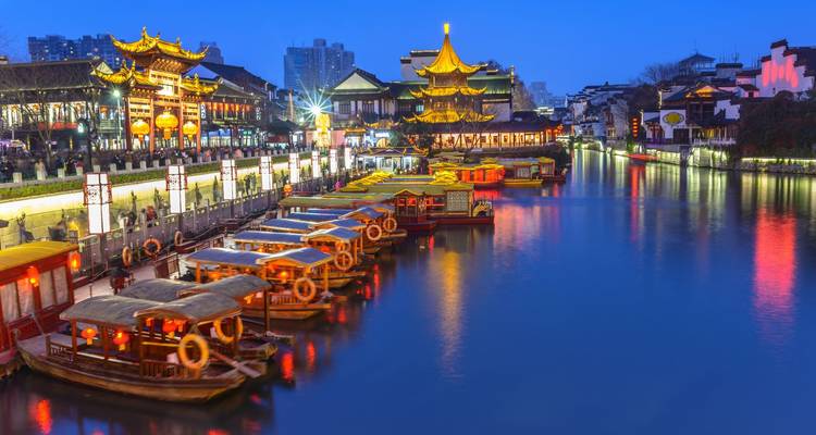 Colorful boats line an illuminated canal in a historic district at blue hour.