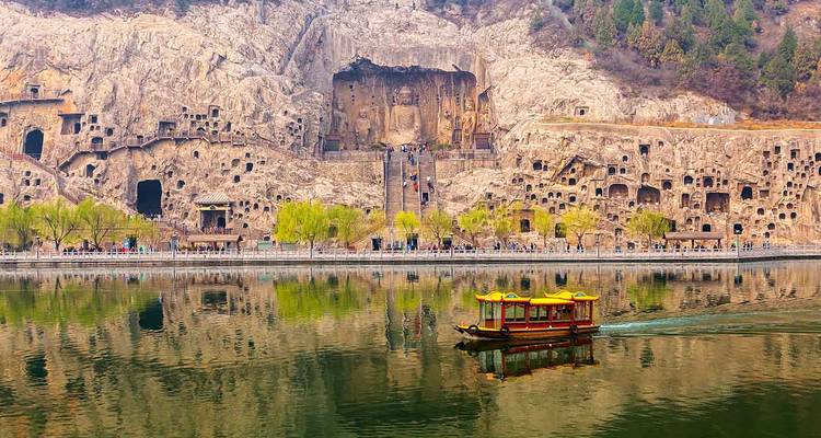 Longmen-grotten, uitgehouwen in de klif met een bootje dat over het kalme water glijdt.