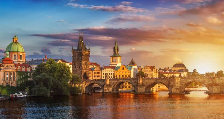 Atardecer dorado sobre el Puente de Carlos de Praga y el horizonte histórico reflejado en el río Moldava.