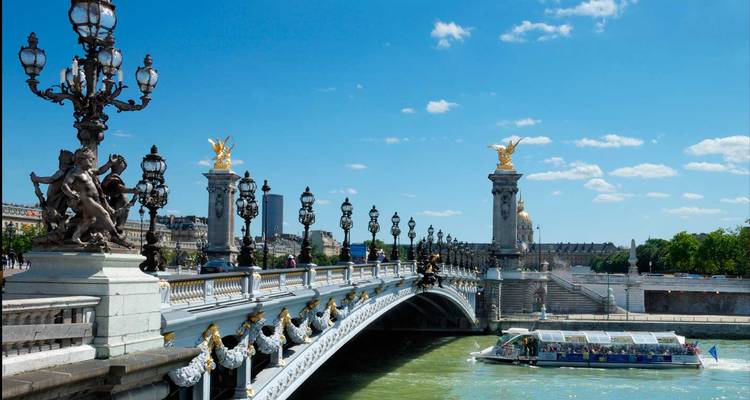 Prächtige Brücke mit vergoldeten Statuen und Ausflugsboot mit Glaskuppel darunter.