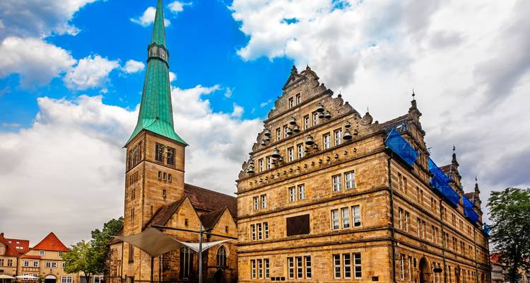 Historisch zandstenen stadhuis en hoge groene spits tegen een gedeeltelijk bewolkte lucht in Hamelen.