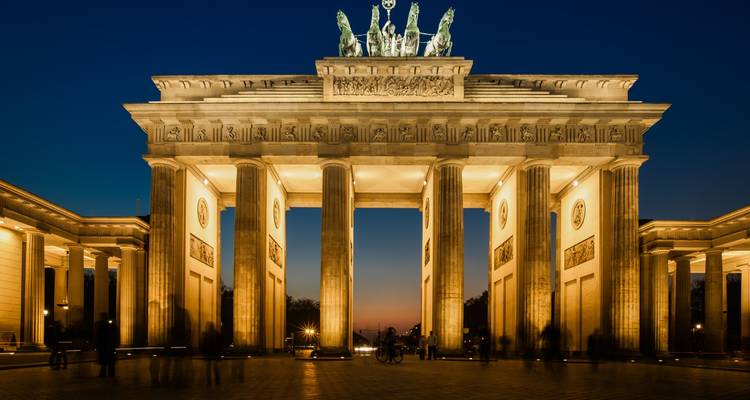 Verlichte Brandenburger Tor 's nachts met een diep blauwe lucht en zachte bewegingsonscherpte van bezoekers.