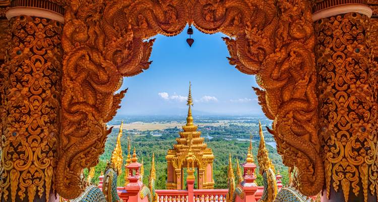Ornate golden temple arch richly carved with dragons framing a sweeping valley and blue sky.