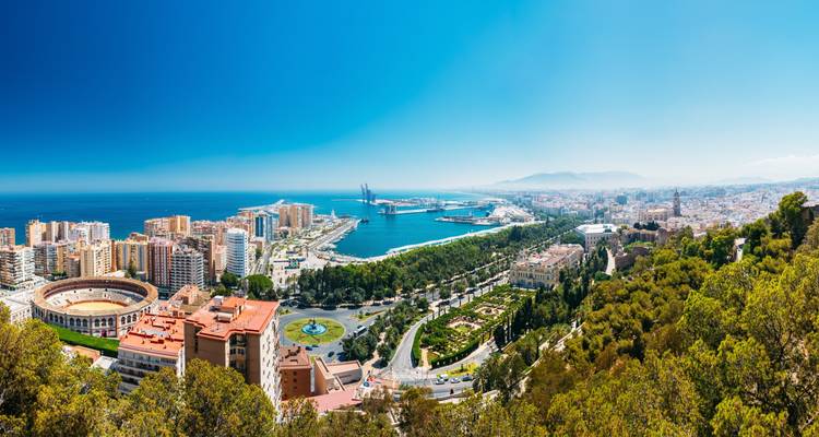 Vue panoramique large de la ville de Málaga, mettant en avant l'arène, les grues du port et la mer bleue scintillante depuis un point de vue élevé.