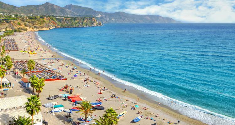 Large plage de sable fin à Nerja avec des baigneurs, des parasols et les eaux turquoise de la Méditerranée.
