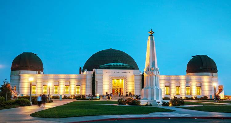 White art-deco observatory glowing with interior lights against a turquoise twilight sky.