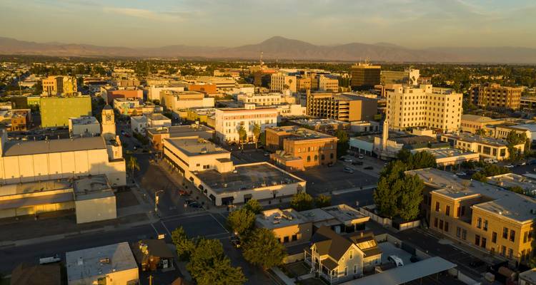 Sunlit small-city downtown with low-rise buildings and mountain backdrop viewed from above.