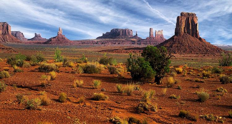 Rugged desert vista with towering red sandstone buttes under streaked blue-white sky.