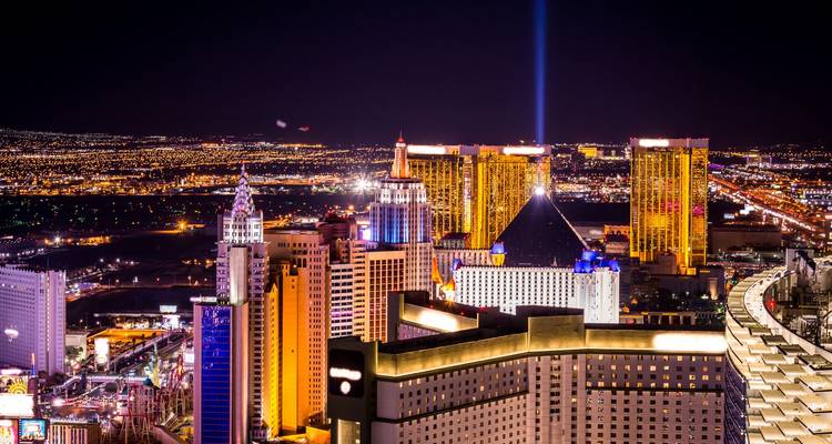 Bright beam of light shoots skyward from neon hotel roofs along a sprawling desert city at night.