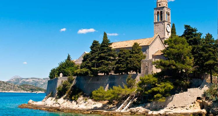 Uferkirche und Glockenturm auf einem felsigen kroatischen Eiland unter klarem blauen Himmel.