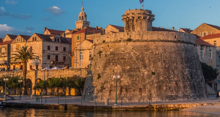 Historischer runder Festungsturm von Korčula, der im warmen Licht des Sonnenuntergangs am Ufer leuchtet.