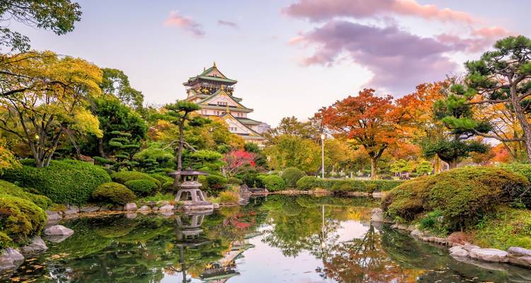 Autumn garden pond reflecting Osaka Castle surrounded by colorful foliage at dusk.
