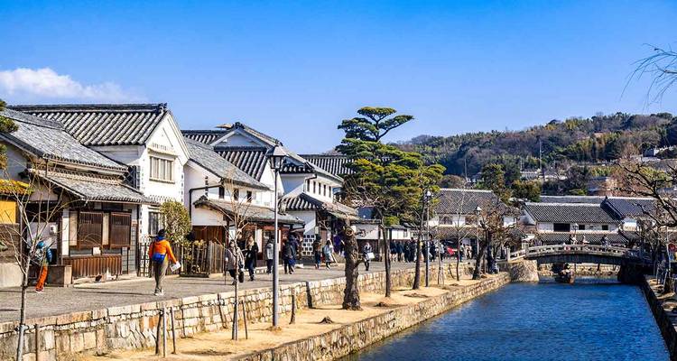 Traditional white-walled buildings and canal walkway in Kurashiki’s historic quarter on sunny day.