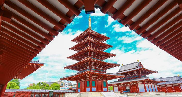 Vibrant five-story pagoda framed by temple eaves against bright blue sky in Nara.