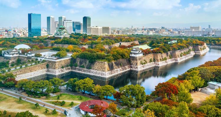 Aerial of Osaka Castle surrounded by expansive moat and modern city skyline.