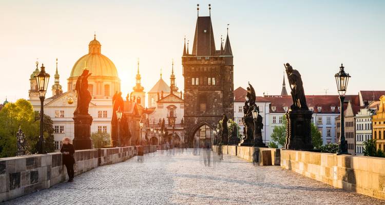 Frühes goldenes Licht auf Prags Karlsbrücke, gesäumt von historischen Statuen und einigen spazierenden Besuchern.
