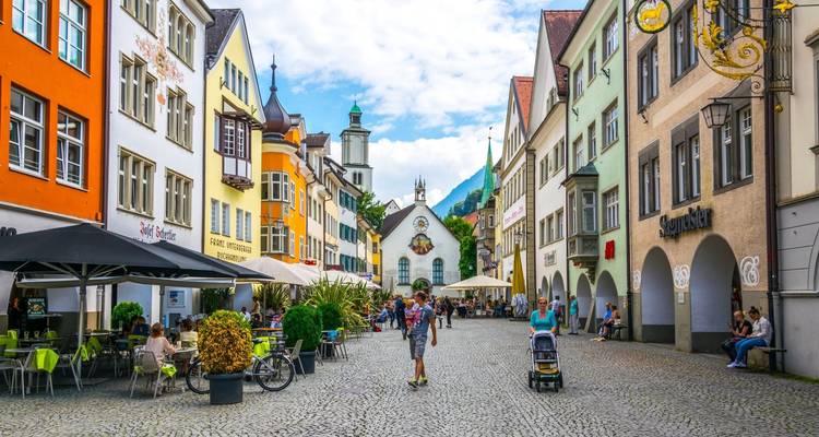 Levendige keitjesstraat in Innsbrucks oude stad met kleurrijke gevels, terrasjes buiten en winkelende mensen met bergen op de achtergrond.