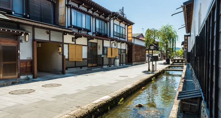 Quiet canal-side street with traditional wooden machiya houses and clear brook in Takayama’s old town.
