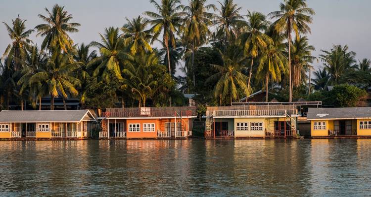 Rangée de maisons d'hôtes colorées flottantes se reflétant dans l'eau calme d'une rivière avec des palmiers en arrière-plan