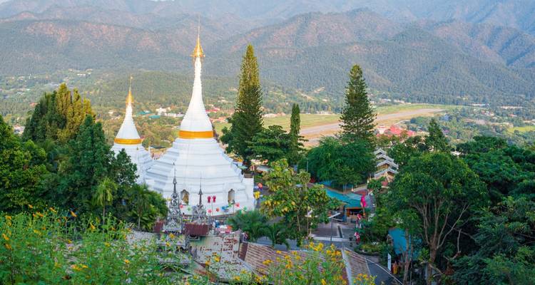 Les stupas blanc et or s'élevant au-dessus de la cime des arbres avec les montagnes en arrière-plan dans le nord de la Thaïlande