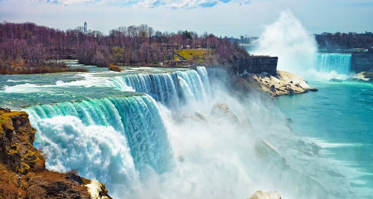 Powerful cascade of Niagara Falls with mist rising high against a backdrop of bare trees.
